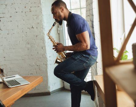 Black man playing the saxophone in front of a computer