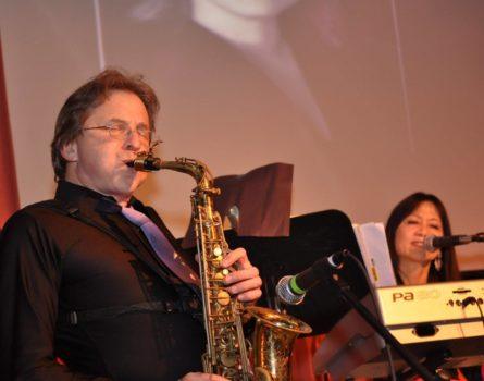 Ernie Mansfield playing the saxophone on stage with his keyboardist in the background